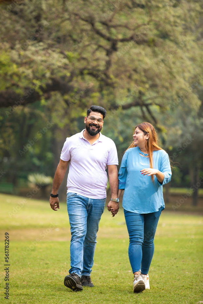 young indian couple holding hand each other and walking in park.
