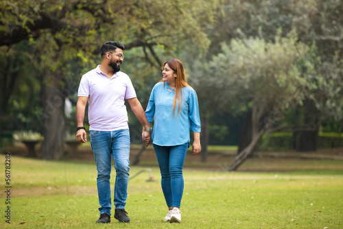 young indian couple holding hand each other and walking in park.