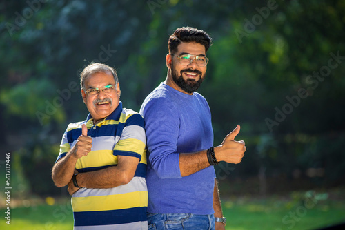 Indian father showing thumps up with young son at park.