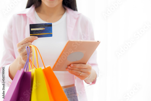 Hands of young asian woman standing using digital tablet shopping online with credit card while holding paper bag, female paying with transaction financial, purchase and payment, business concept.