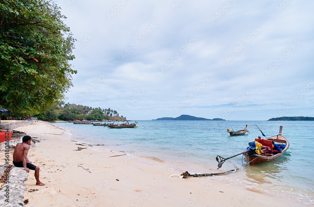 Fisher man on the sand beach with traditional longtail boats.