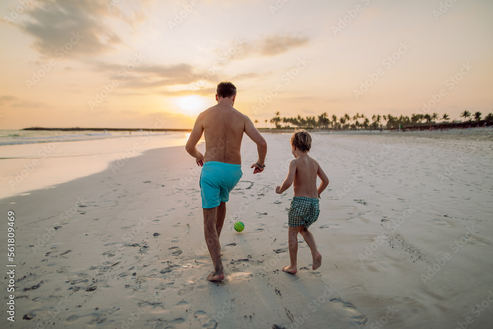 Rear view of father with his son plaing football on the beach.