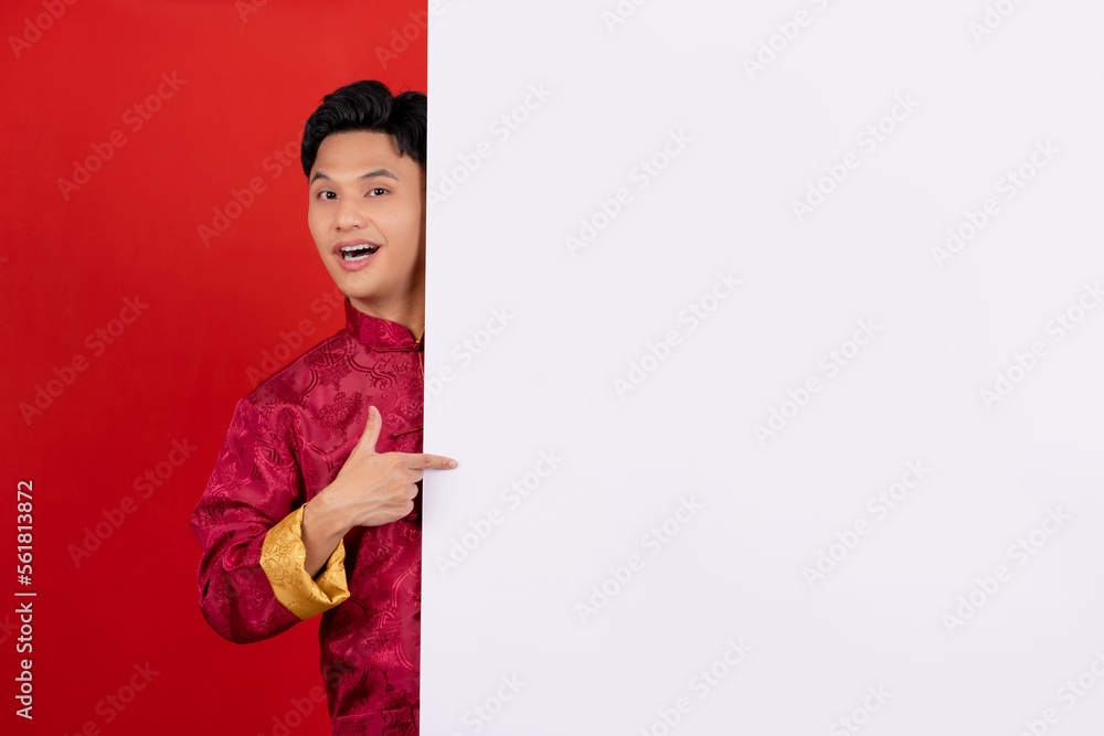 Happy handsome asian man wearing traditional cheongsam qipao with hand pointing blank announcement banner in red background. Happy handsome asian man wearing traditional cheongsam qipao with hand pointing blank announcement banner in red background.