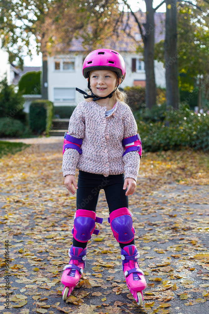 Fototapeta premium Smiling child girl in a helmet in protection rollerblades in the park