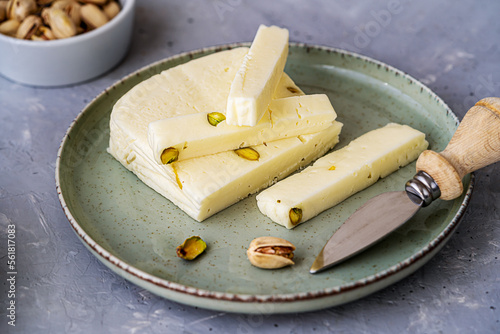 Italian cheese asiago with pistachios on stone black cutting board with cheese knife, pistachios in bowl and green napkin photo