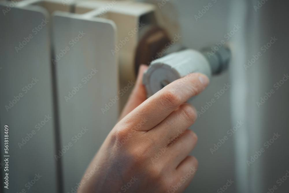 Female hand adjusting thermostat to turn on the radiator heater at home.