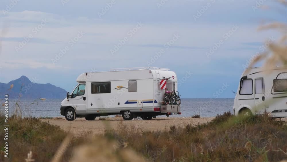 Parked Campervans And Passing Cyclists On The Sea Beach Parked Campervans And Passing Cyclists On The Sea Beach