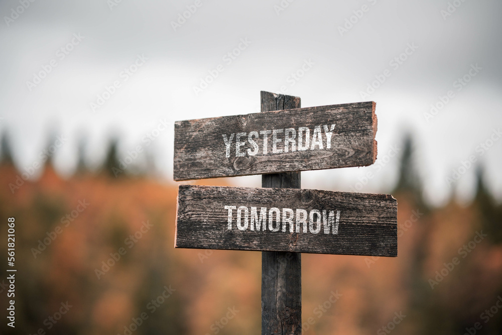 vintage and rustic wooden signpost with the weathered text quote yesterday tomorrow, outdoors in nature. blurred out forest fall colors in the background.