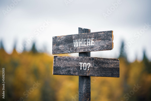 vintage and rustic wooden signpost with the weathered text quote where to, outdoors in nature. blurred out forest fall colors in the background.
