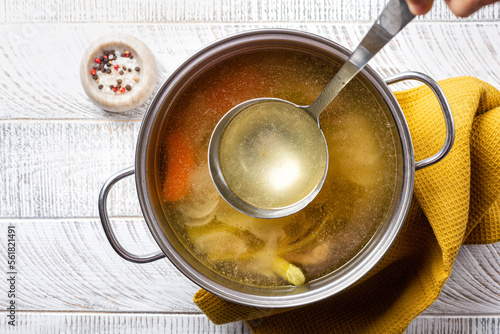 Foto Cooking beef broth stock in a saucepan with a ladle , made using meat, bones, vegetables, carrot, onin, celery, and seasoning