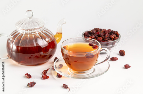 A cup of brewed rosehip medicinal plants herbal tea on a white table with dried rosehips