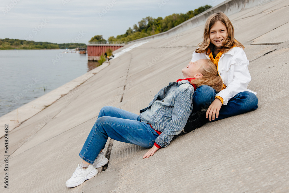 Fototapeta premium Two schoolmates relax and have fun on concrete embankment.