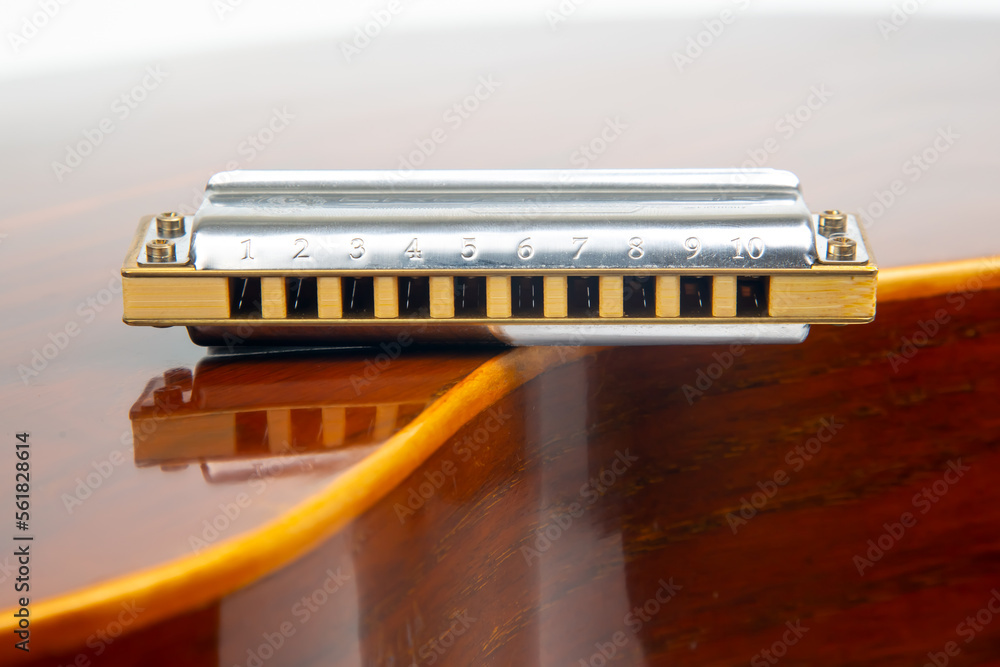The harmonica rests on the body of a classical guitar. Classical musical wind instrument. The harmonica rests on the body of a classical guitar. Classical musical wind instrument.