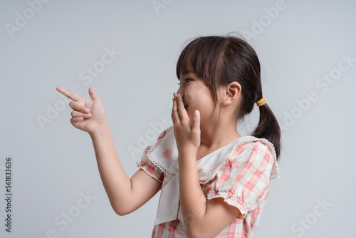 Child with gesture smells bad. Child covers nose with hand, smells something awful, pinches nose, frowns in displeasure and pointing finger to camera. Teenager showing that something stinks. photo