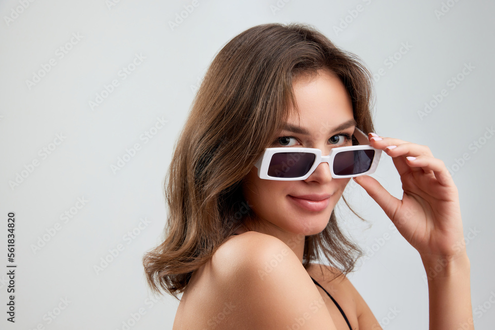 Portrait of young stylish beautiful girl in fashionable eyewear isolated over grey background. Concept of beauty, skin care, cosmetology, fashion, makeup Portrait of young stylish beautiful girl in fashionable eyewear isolated over grey background. Concept of beauty, skin care, cosmetology, fashion, makeup
