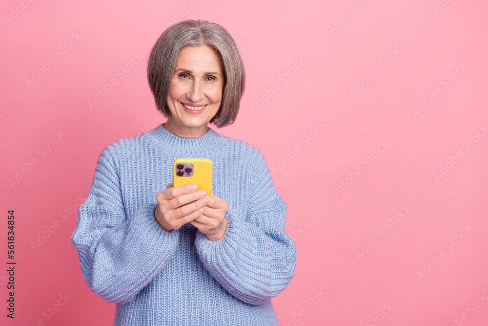 Photo portrait of positive smile pensioner woman enjoy online shopping hold phone promo season sale black friday isolated on pink color background Photo portrait of positive smile pensioner woman enjoy online shopping hold phone promo season sale black friday isolated on pink color background