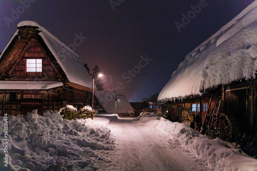 Snow piles along cleared road by traditional wooden houses in village at night