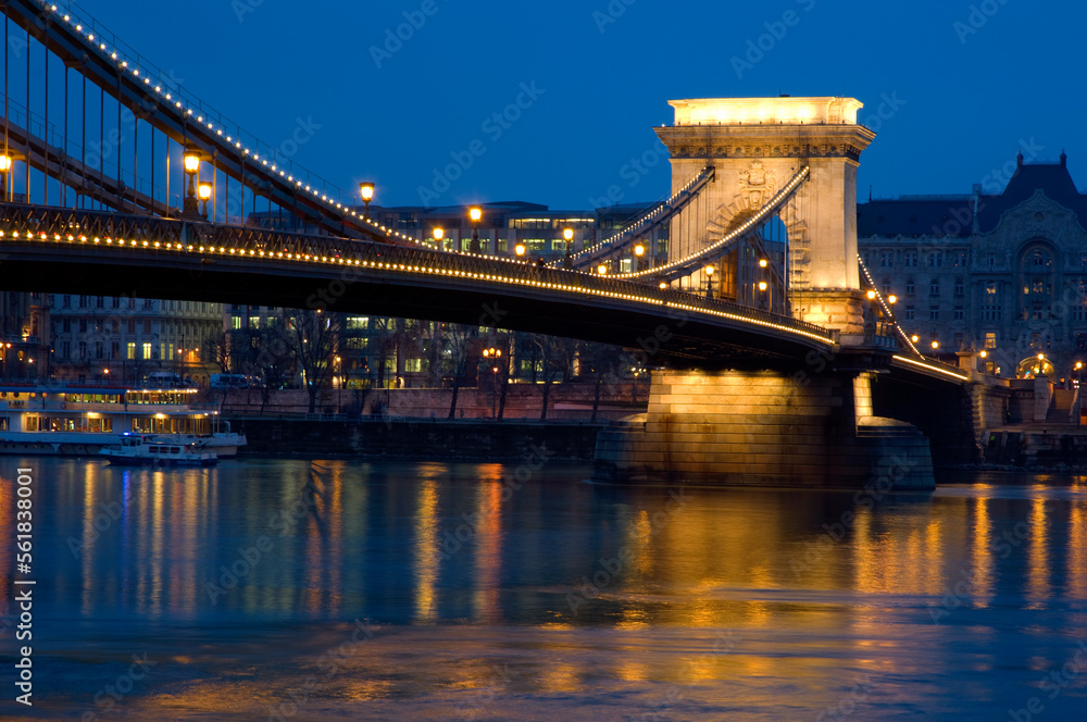 The Chain Bridge, Budapest, Hungary.  Looking towards Pest, night time.  Lighte reflected in the water of the Danube.