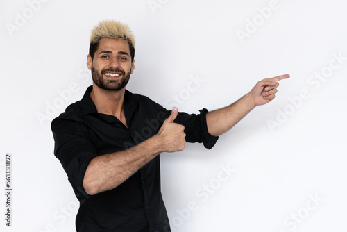 Cheerful young man pointing at copyspace and showing thumb up. Male Caucasian model with brown eyes, ombre painted hair and beard in black shirt recommending advertisement. Advertising, review concept