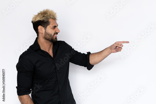 Irritated young man pointing at copyspace. Male Caucasian model with brown eyes, ombre painted hair and beard in black shirt looking aside showing displeasure. Negative emotion, advertising concept