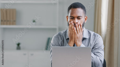 Stressed shocked African American ethnic bearded adult man office worker businessman with laptop computer sad upset frustrated reading online bad news mistake service error failure business problem photo