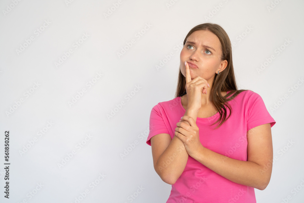 Doubtful young woman rubbing chin. Portrait of pensive Caucasian female model with brown hair in pink T-shirt looking away at ads, pouting lips, considering special offer. Advertisement concept Doubtful young woman rubbing chin. Portrait of pensive Caucasian female model with brown hair in pink T-shirt looking away at ads, pouting lips, considering special offer. Advertisement concept