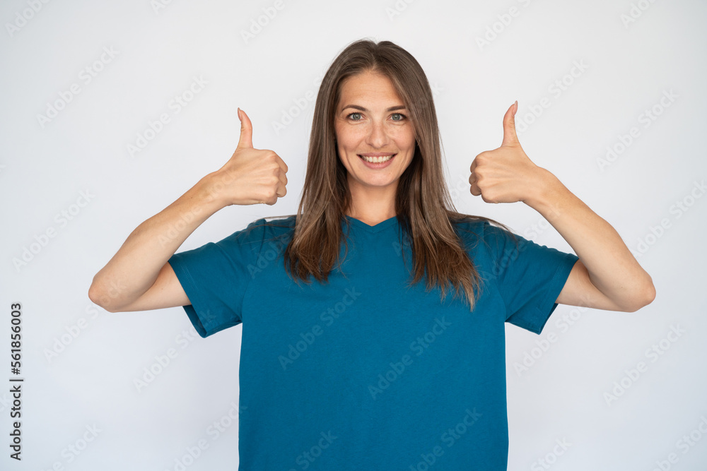 Happy Caucasian woman with thumbs up. Portrait of cheerful young female model with brown hair in blue T-shirt looking at camera, smiling and approving message or product. Like, advertisement concept Happy Caucasian woman with thumbs up. Portrait of cheerful young female model with brown hair in blue T-shirt looking at camera, smiling and approving message or product. Like, advertisement concept