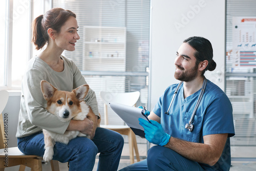 Young male veterinarian with medical document talking to owner of pet photo