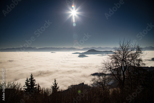 the sun standing high in the sky above a sea of clouds during a inversive weather situation in carinthia austria.