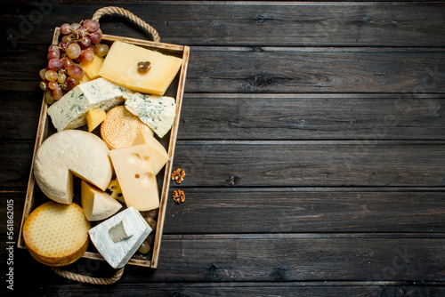 Different types of cheese in a wooden tray with grapes .