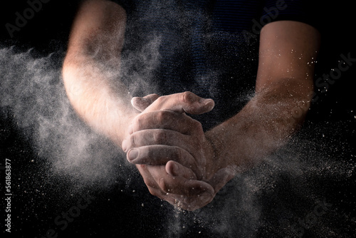Explosion of flour in male hands on a dark background. Dough preparation, cooking concept.