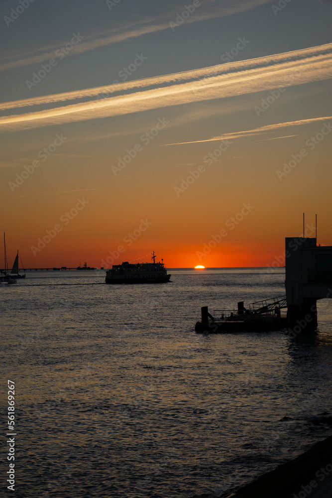 sunset with a silhouetted boat sailing just out of  port along its journey against a vivid colorful sunset an orange and yellow color filled sky.
