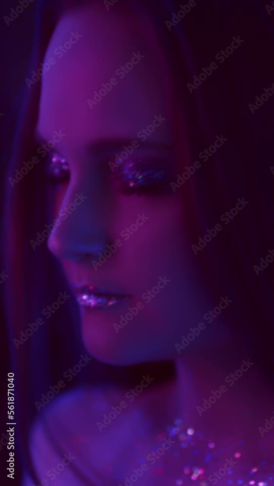 Vertical video. Neon girl. Glitter makeup. Nightclub beauty. Purple color light relaxed woman with sparkling face skin eyeshadow lips dancing with closed eyes on dark. Vertical video. Neon girl. Glitter makeup. Nightclub beauty. Purple color light relaxed woman with sparkling face skin eyeshadow lips dancing with closed eyes on dark.