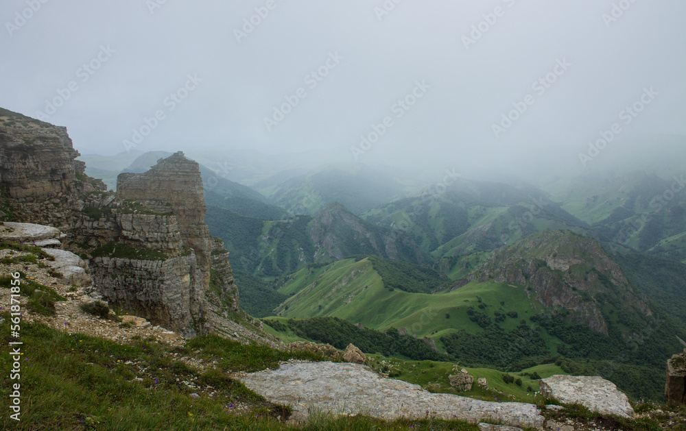Dramatic landscape - panoramic view of the hilly valley from the Bermamyt plateau in Karachay-Cherkessia in a misty haze and stone cliffs