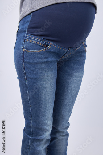Pregnant woman in blue jeans on a gray background, jeans model for pregnant women