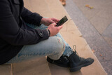 Close-up of a man looking at his phone sitting on stairs in the street