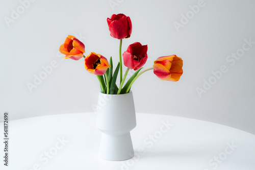Bouquet of red and yellow tulips in a white vase on a light grey background.