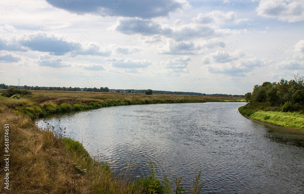 Pastoral landscape - a beautiful bend of the Klyazma River in a meadow with grass and a tree with lush green foliage and a cloudy sky with space to copy in the Moscow region Pastoral landscape - a beautiful bend of the Klyazma River in a meadow with grass and a tree with lush green foliage and a cloudy sky with space to copy in the Moscow region