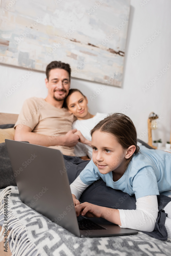 positive kid using laptop near happy parents on blurred background. positive kid using laptop near happy parents on blurred background.