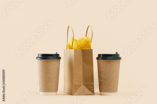 Takeaway two paper coffee cups with lunch bag on beige. Snack delivery service. Coffee to go. Grab and go or carry out beverage. Disposable mockup packaging. pair. Minimal photo