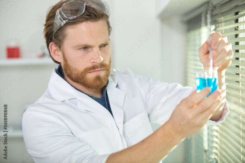 scientist holds a beaker in his laboratory beside the window scientist holds a beaker in his laboratory beside the window