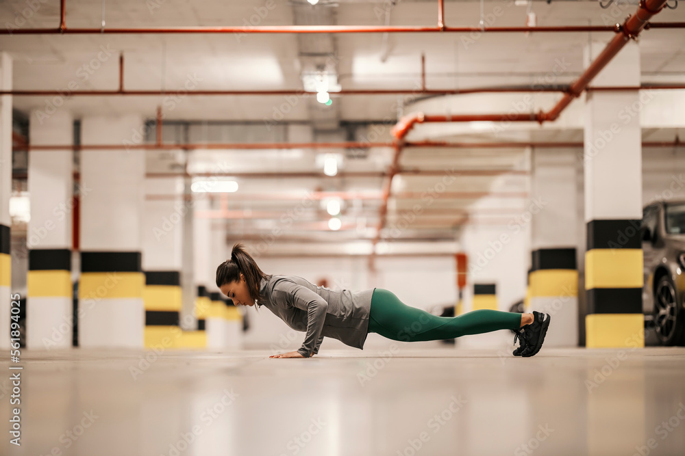 Muscular, strong sportswoman is doing pushups in underground garage.