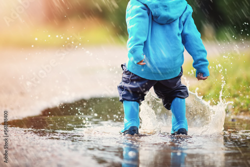 Small child jumping through puddles in nature in spring