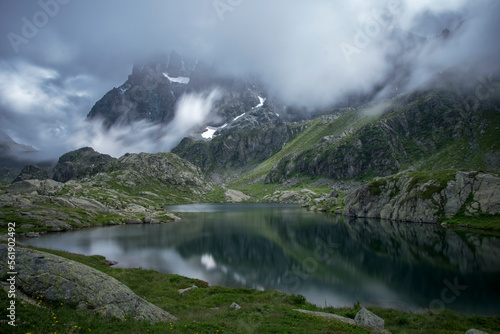 Obraz na płótnie Alpine lake with mountain (Monviso, Mount Viso, 3841 m) in the background reflecting in its clear Waters, and passing fast clouds, long exposure, Piedmont, Italian alps. w salonie