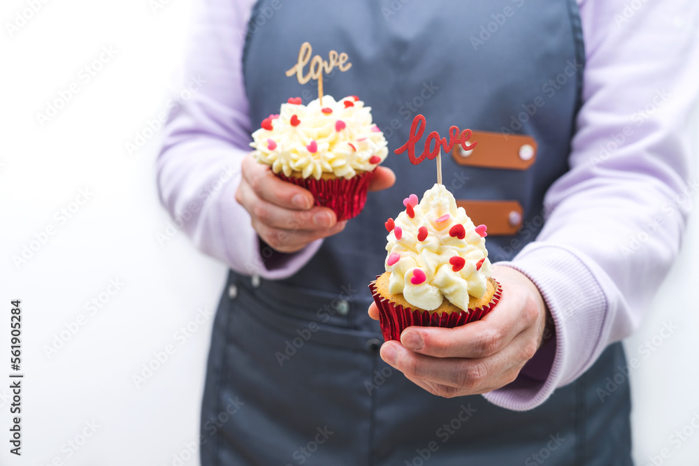 Woman waitress with two cupcakes decorated with red hearts topping and wooden sign with LOVE letters. Valentine's Day. White background. Woman waitress with two cupcakes decorated with red hearts topping and wooden sign with LOVE letters. Valentine's Day. White background.