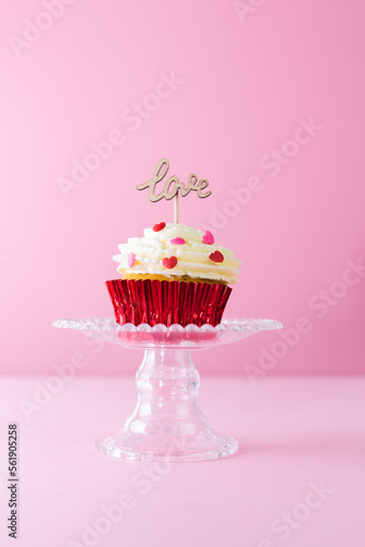 Valentine s Day. A cupcake with cream and red topping decoration with a wooden sign with the word LOVE on a pink background. Vertical photo.