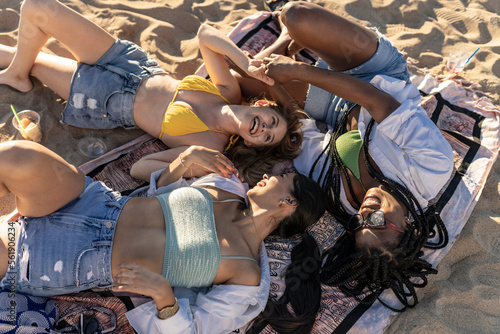multiracial female friends lying on beach sand having fun