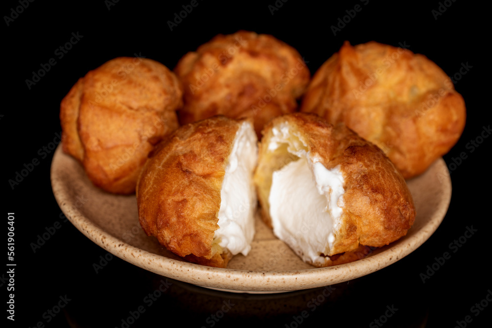 Tasty chouquettes with cream on a saucer, on a black background.