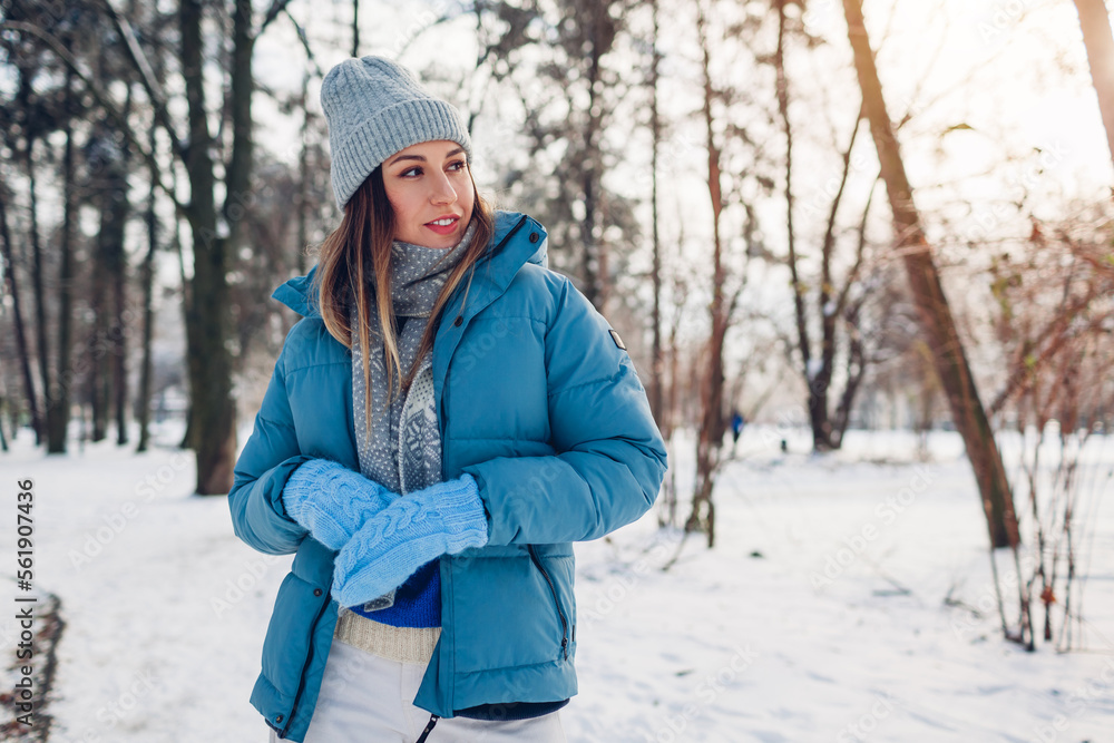 Young woman walking in snowy winter park wearing blue coat. Girl enjoys landscape wearing hat and mittens Young woman walking in snowy winter park wearing blue coat. Girl enjoys landscape wearing hat and mittens