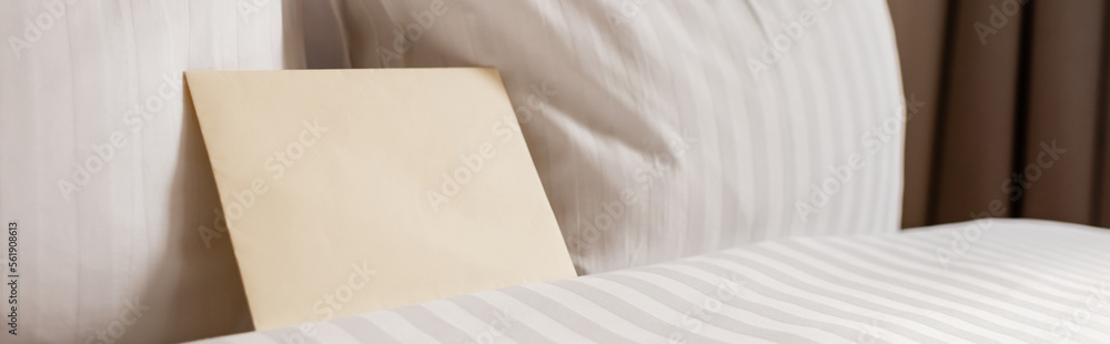 blank envelope on white and clean bedding in hotel room, banner.